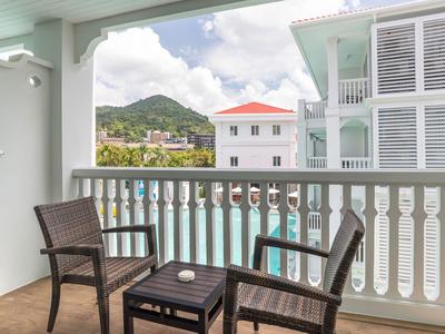 Balkon mit Stühlen und Tisch mit Blick auf Pool und umliegende Gebäude und Hügel.