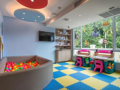 Bunter Kinderspielraum mit Bällebad, Spieltischen und großen Fenstern mit Blick ins Grüne.