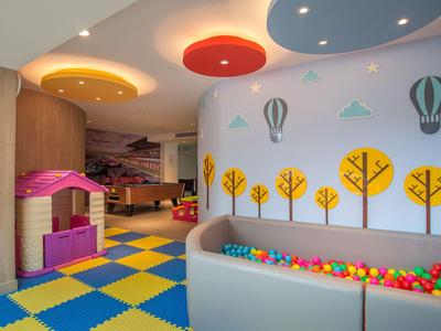 Bunter Kinderspielraum mit Bällebad, farbigen Deckenplatten und Wanddekoration mit Heißluftballons und Bäumen.