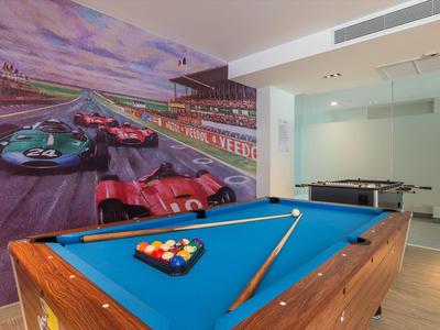 Billardtisch mit blauer Filzoberfläche in einem Raum mit Autorennbahn-Wandgemälde und Pokerautomaten.