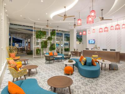 Modernes Hotellobby mit blauen Sofas, orangefarbenen Kissen und hängenden roten Lampen.