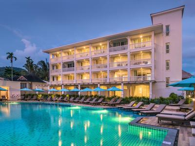 Modernes Hotel mit beleuchtetem Pool und Liegestühlen bei Abenddämmerung