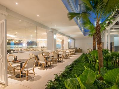 Eleganter Außenbereich eines Restaurants mit Tischen, Stühlen und üppiger Pflanzenbegrünung bei Nacht.