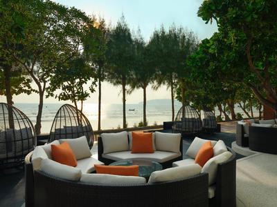 Gemütliche, runde Sitzgruppe mit weißen Kissen und orangefarbenen Akzenten auf einer Terrasse mit Meerblick.