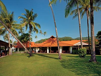 Großes Haus mit roten Dächern umgeben von hohen Palmen und grünem, gepflegtem Rasen.