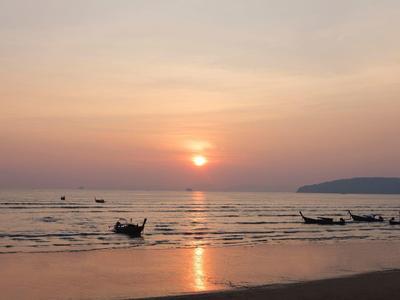 Sonnenuntergang über ruhigem Meer mit traditionellen Booten und leicht bewölktem Himmel.