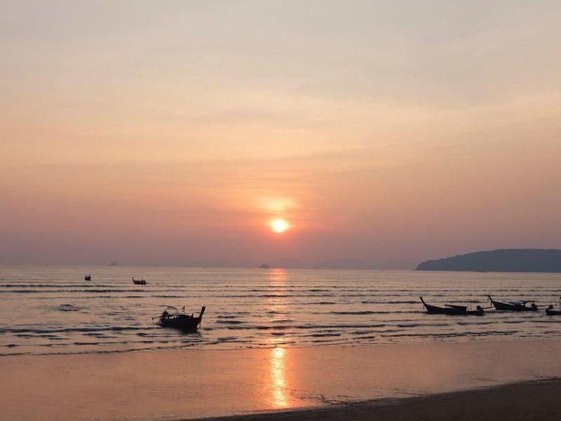 Sonnenuntergang über ruhigem Meer mit traditionellen Booten und leicht bewölktem Himmel.
