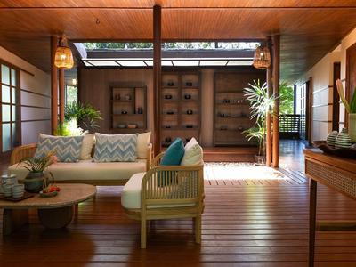 Helles Wohnzimmer mit Holzboden, Rattansofa, Teetisch und großen Pflanzen, offen zum Außenbereich.