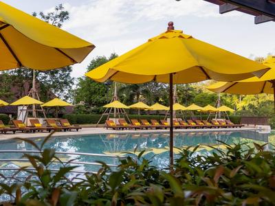 Poolbereich mit gelben Sonnenschirmen und Liegestühlen, umgeben von grüner Landschaft.