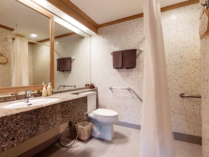 Helles Badezimmer mit großer Spiegelwand, Marmorwaschbecken, WC und Duschvorhang auf der rechten Seite.