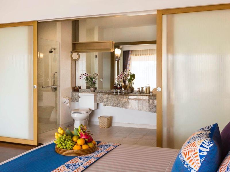 Helles Badezimmer mit großer Spiegelwand neben modernem Schlafzimmer mit bunten Kissen.