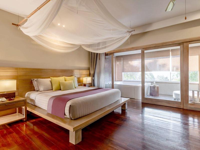 Modernes Hotelzimmer mit Doppelbett, Holzboden und Balkon mit Sitzgelegenheit.