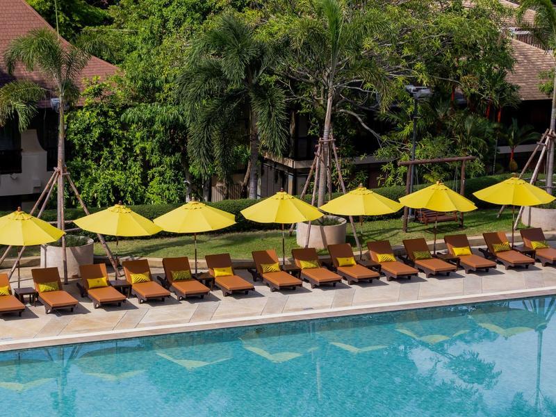 Reihe aus gelben Sonnenschirmen und Holzliegen neben klarem blauen Schwimmbecken.