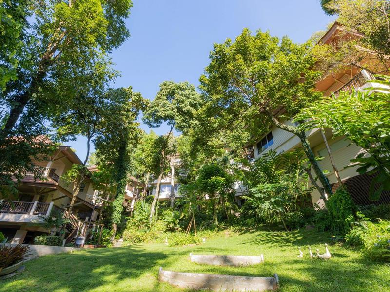 Grüne Gartenanlage mit Bäumen zwischen mehrstöckigen Hotelgebäuden an einem sonnigen Tag.