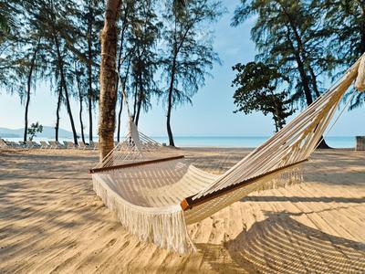 Leere Hängematte zwischen Bäumen am sonnigen Sandstrand mit klarem blauem Himmel.