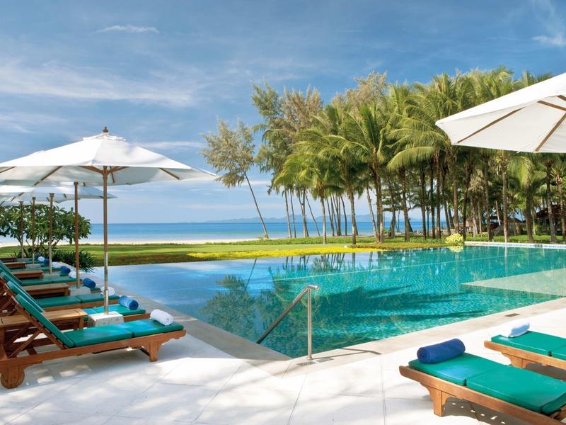 Swimmingpool mit Liegestühlen und Sonnenschirmen neben Palmen und Blick aufs Meer