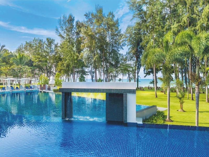 Großer blauer Pool mit modernem Pavillon und Palmen auf grünem Rasen unter blauem Himmel.