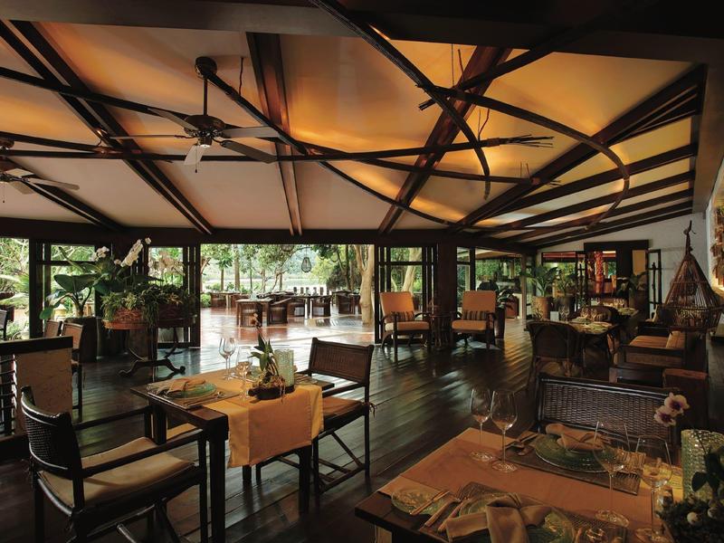 Geräumiges Restaurant mit Holzstuhlgruppen, dunklem Holzboden und großer Glasfront zur Natur.