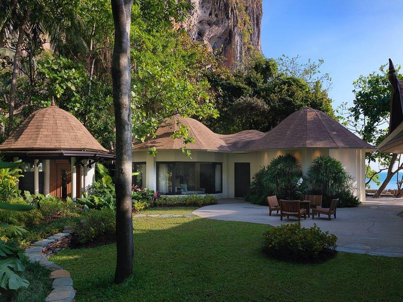 Großes Haus mit runden Dächern, umgeben von Bäumen und gepflegtem Garten unter blauem Himmel.