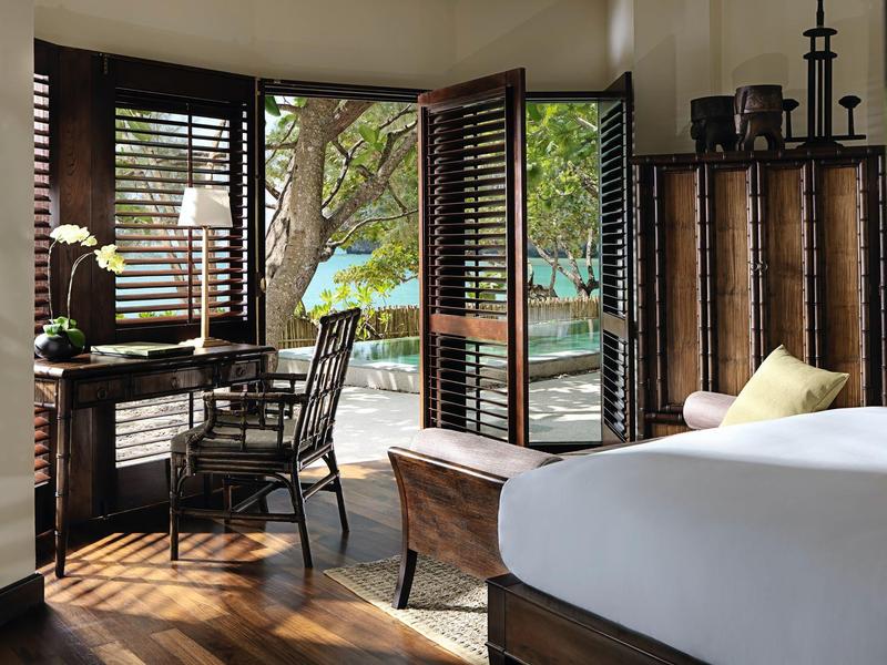 Helles Schlafzimmer mit Holzboden, Schreibtisch, Stuhl und offener Tür zum Balkon mit Meerblick.