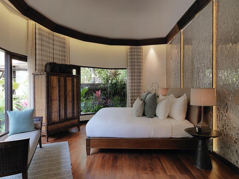 Modernes Schlafzimmer mit großem Bett, Holzmöbeln und großen Fenstern mit Blick ins Grüne.