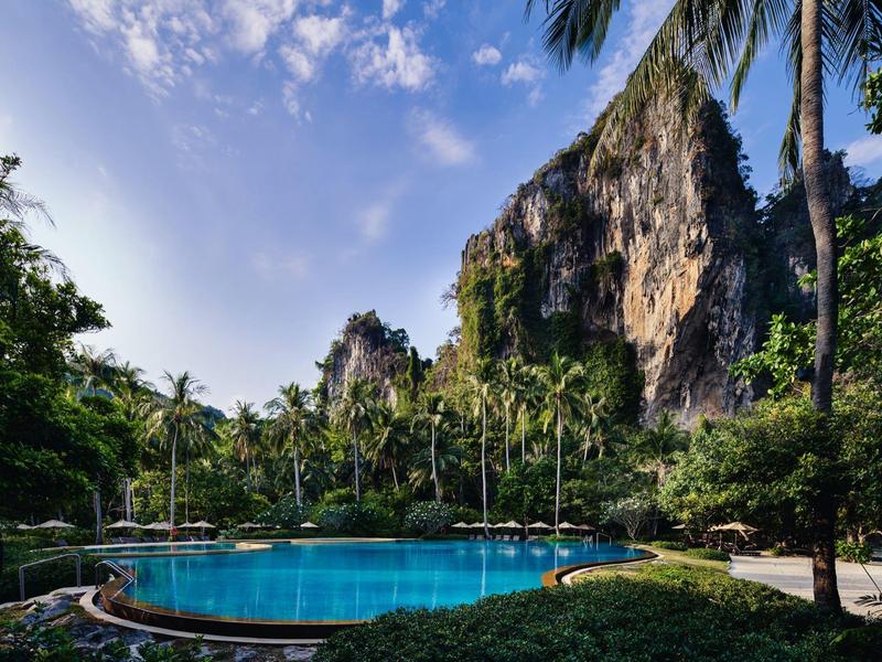Runder Pool umgeben von Palmen und Felsen unter blauem Himmel in tropischer Umgebung.