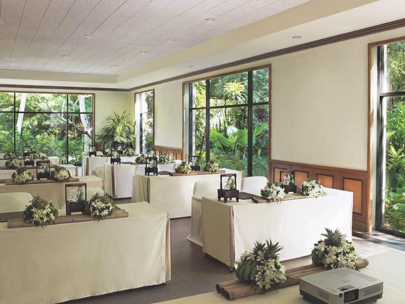 Hell erleuchteter Raum mit großen Fenstern, rechteckigen Tischen und modernen Dekorationen in Weiß und Grün.