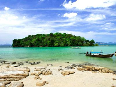 Türkisfarbenes Meer, grüner bewaldeter Inselhügel, weißer Sandstrand mit Steinen, kleines Boot am Ufer.