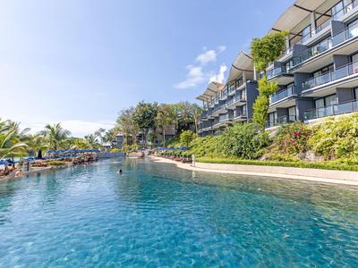 Großer Hotelpool mit Liegestühlen und Pflanzen unter klarem Himmel.