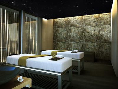 Dunkler Raum mit zwei Massageliegen, Steinwand, sanfter Beleuchtung und Schleiervorhängen.