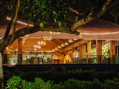 Gemütliches, beleuchtetes Restaurant mit Holzdecke und großem Fenster in tropischer Nacht.