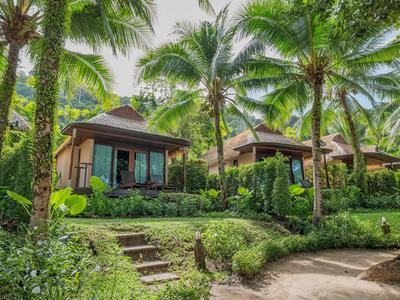 Zwei kleine Bungalows umgeben von tropischen Palmen und üppigem Grün.