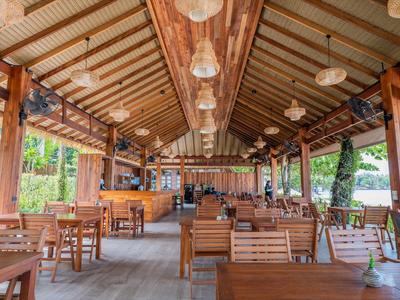 Offener Restaurantsaal mit Holzmöbeln und Sicht auf Garten und See.