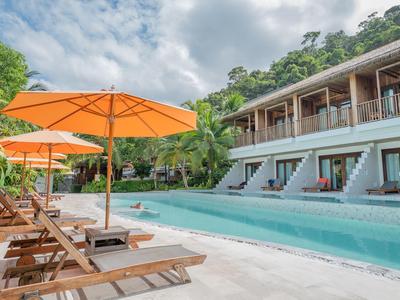 Hotelpool mit Liegestühlen und orangen Sonnenschirmen neben einem zweistöckigen Gebäude im Grünen.