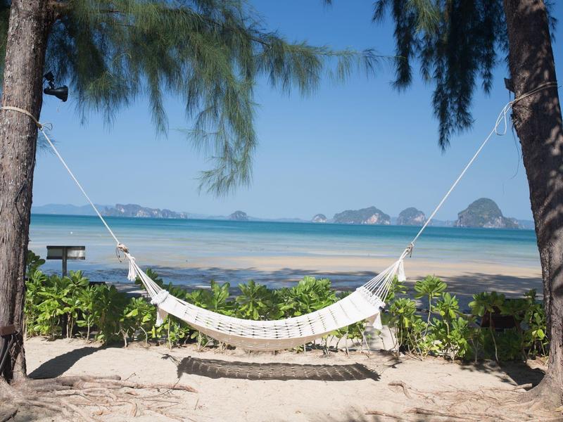 Hängematte zwischen zwei Bäumen am Sandstrand mit Blick auf blaues Meer und Himmel.