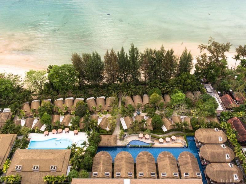 Luftaufnahme eines Resorts mit Pool, Bungalows und Blick auf einen Sandstrand mit grünem Wasser