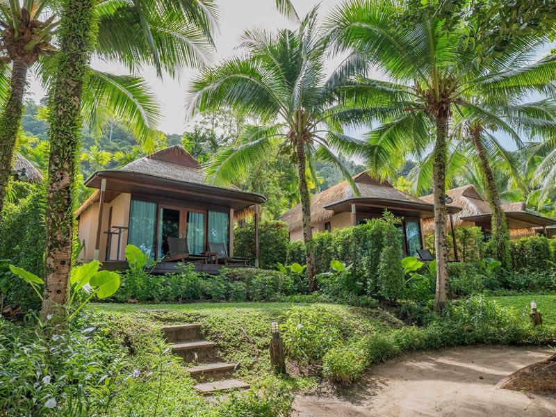 Tropische Ferienbungalows umgeben von Palmen und üppigem Grün mit sonnigem Himmel.
