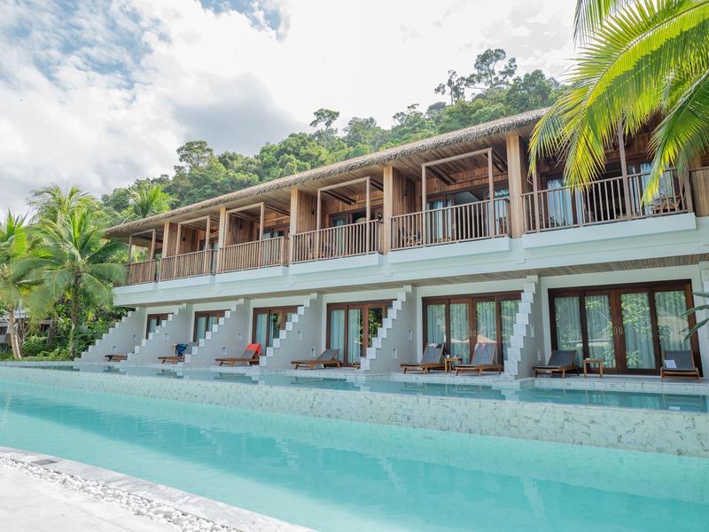 Modernes Hotel mit Pool und Balkonen vor üppiger grüner Landschaft.
