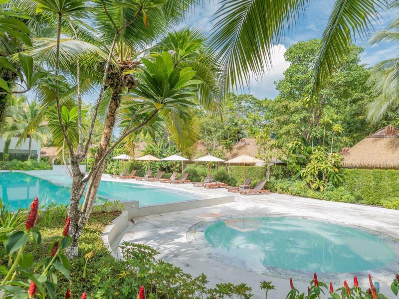 Ein tropischer Pool- und Whirlpoolbereich mit Palmen und Sonnenschirmen.