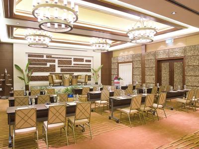 Großer, heller Konferenzraum mit Teppichboden, rechteckigen Tischen und modernen Kronleuchtern.