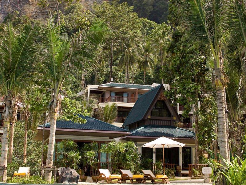 Moderner Bungalow mit Pool, umgeben von Palmen und hohen Felsen im Hintergrund.