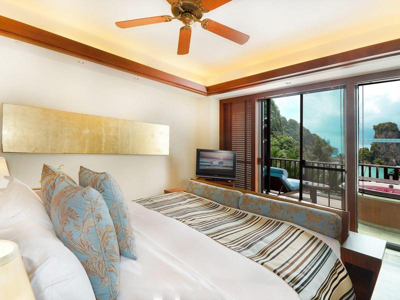 Helles Schlafzimmer mit großem Bett, Deckenventilator, Balkon und Blick auf Wald und Felsen.