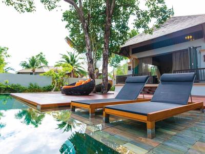 Moderner Garten mit Holzterrasse, Liegestühlen, Pool und Haus im Grünen an sonnigem Tag.