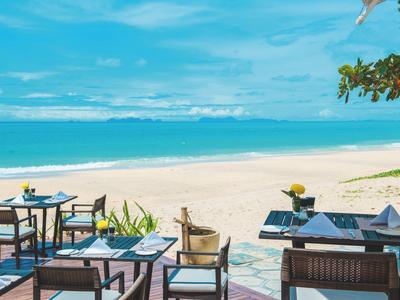 Terrasse mit Tischen und Stühlen am weißen Sandstrand mit Blick auf das blaue Meer.