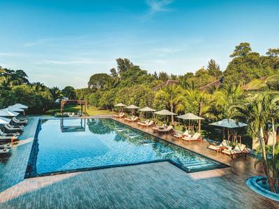 Großer Außenpool mit blauer Wasseroberfläche, umgeben von Liegestühlen und grünen Palmen.