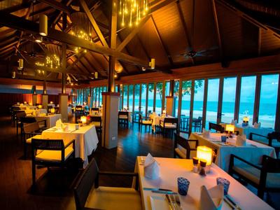 Elegantes Restaurant mit Holzdach, gedeckten Tischen und großem Meerblick bei Dämmerung.