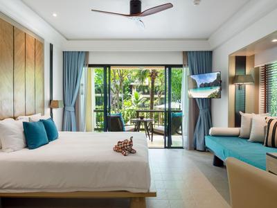 Habitación de hotel moderna con cama doble, sofá, ventilador de techo y vista a terraza con jardín.