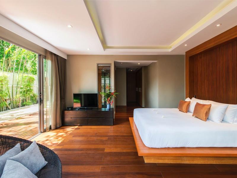 Modernes Schlafzimmer mit großem Bett, Holzboden, Sitzbereich und bodentiefen Fenstern zur Terrasse.