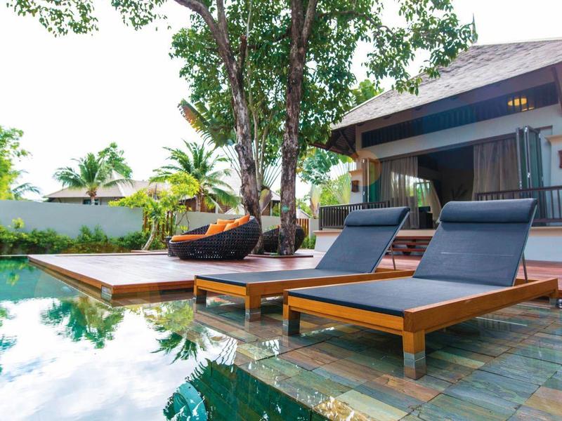 Moderner Garten mit Holzterrasse, Liegestühlen, Pool und Haus im Grünen an sonnigem Tag.