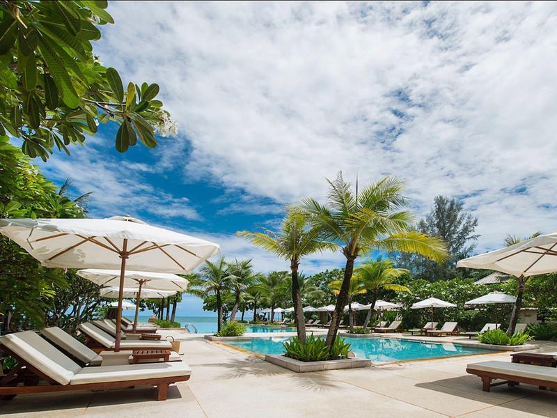 Luxuriöser Poolbereich mit Liegestühlen, Sonnenschirmen, Palmen und blauem Himmel.